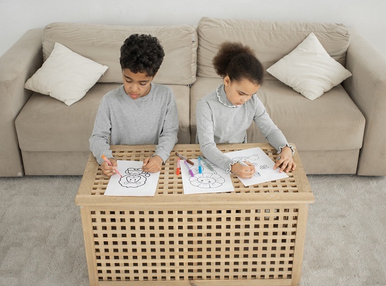 Children sitting on carpeted living room floor while coloring at wooden table