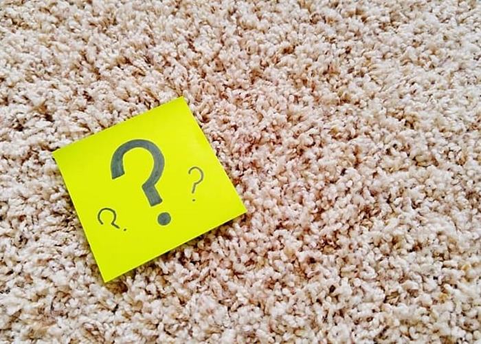 Yellow Post-It note with black question mark on beige carpeting
