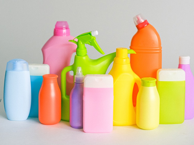 Twelve cleaning solution bottles in assorted colors on white surface