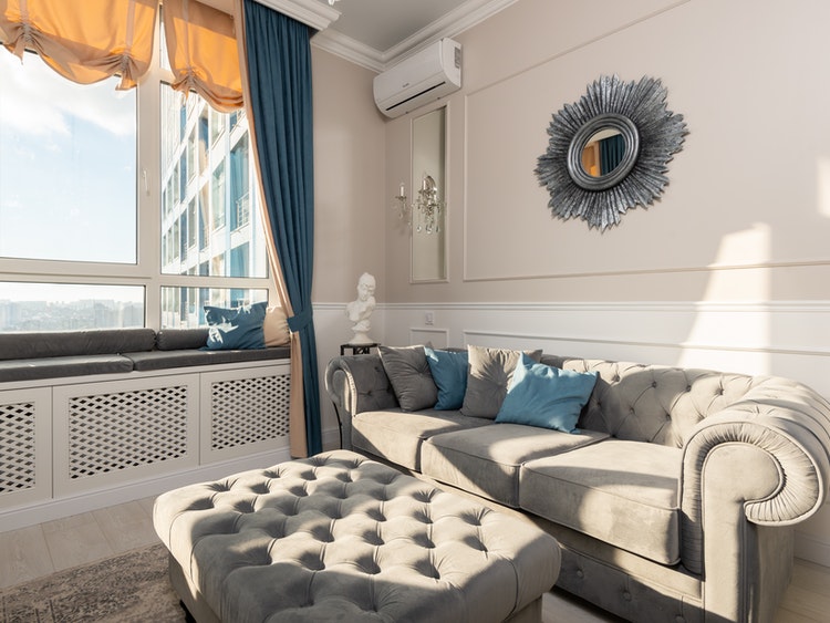 Sunlit living room with beige rug and white upholstered sofa with blue throw pillows