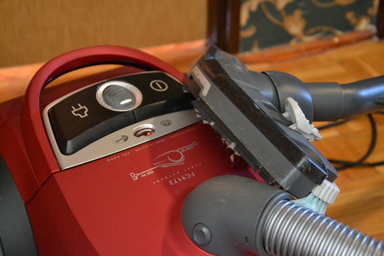 Red vacuum cleaner with hose attachment on hardwood floor