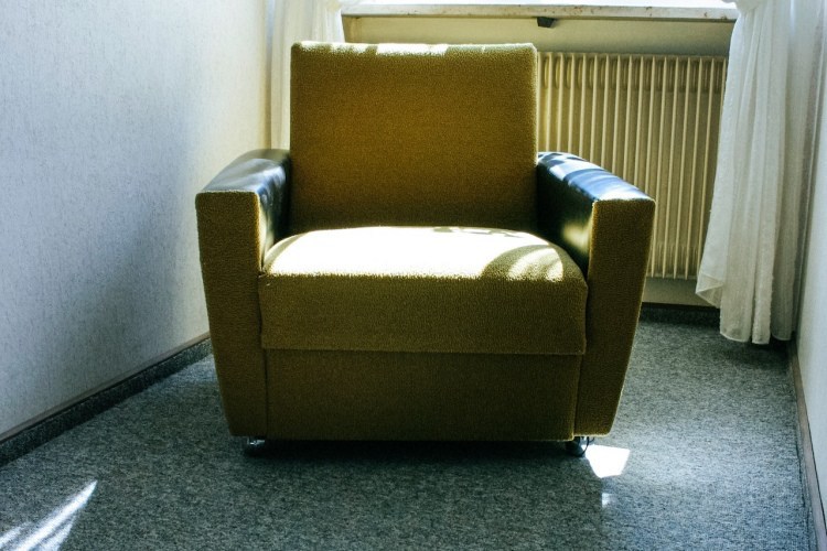 Yellow recliner chair in living room with wall-mounted furnace and blue carpeting