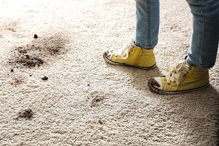 Man in muddy boots leaving footprints on dirty white carpeting