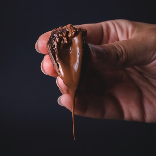Hand holding dark chocolate candy with dripping milk chocolate center