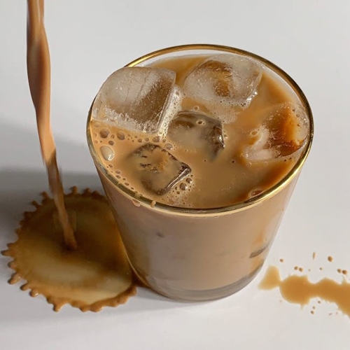 Coffee pouring onto white table beside iced coffee glass