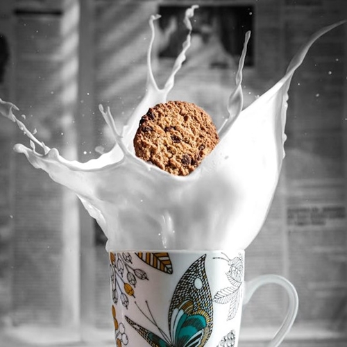 Milk and oatmeal cookie splashing upward from painted coffee mug