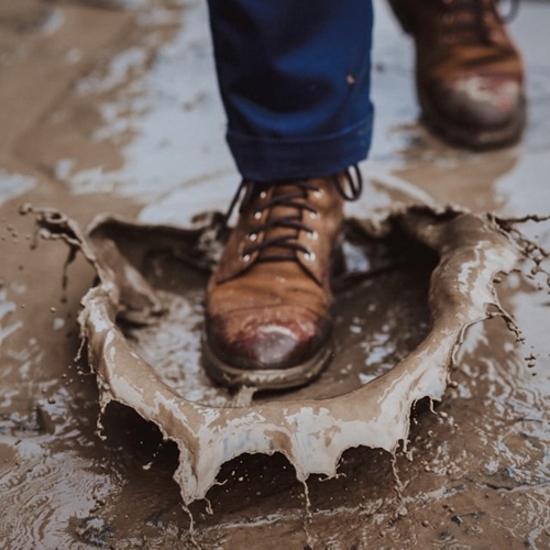 Brown hiking boots stepping into splashing mud puddle
