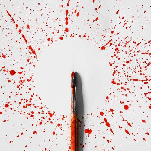 Red paint splattered across white surface surrounding narrow paintbrush