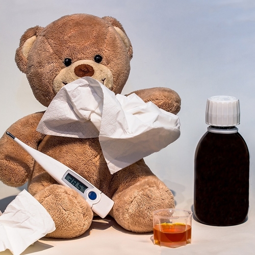 Sick teddy bear with tissues, thermometer, and liquid cold medicine