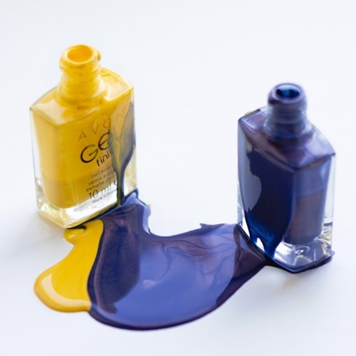 Spilled yellow and purple nail polish beside polish bottles