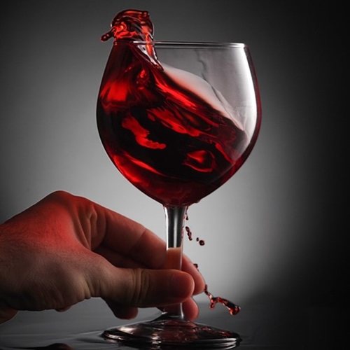 Hand holding stem of wine glass with red wine splashing over edge