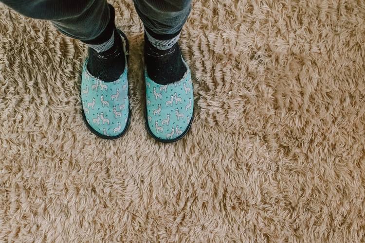 Person in light blue slippers on beige crunchy carpeting