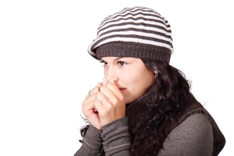 Woman shivering inside cold room wearing winter hat, long-sleeved shirt and winter vest