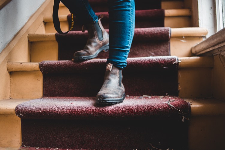 Woman in white sneakers and jeans walking down stairs with dirty red carpet covering