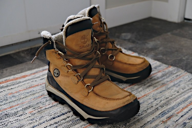 Light brown leather lace-up boots on rug beside front door in tiled residential entryway