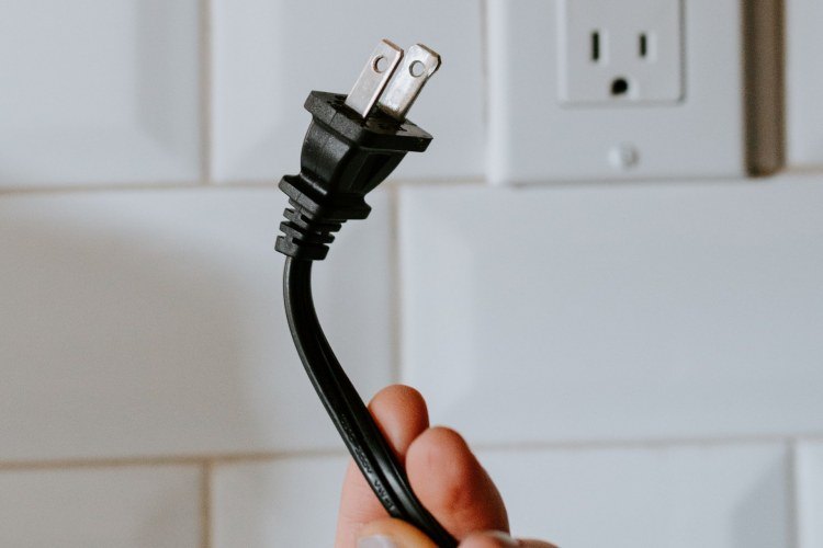 Hand holding unplugged black electrical cord near electrical outlet in residential kitchen