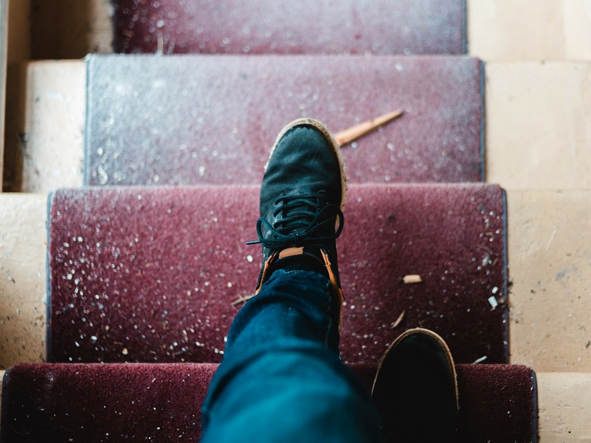Man in black sneakers walking down staircase with dirty red carpeting