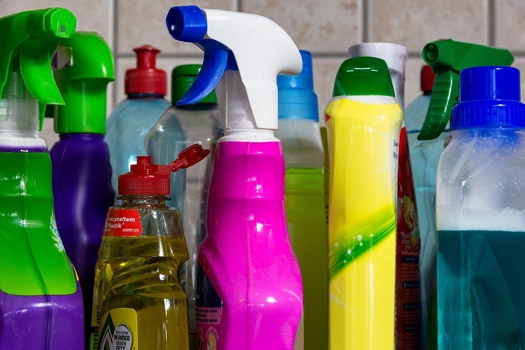 Assorted bottles of cleaning supplies on kitchen countertop beside tiled backsplash