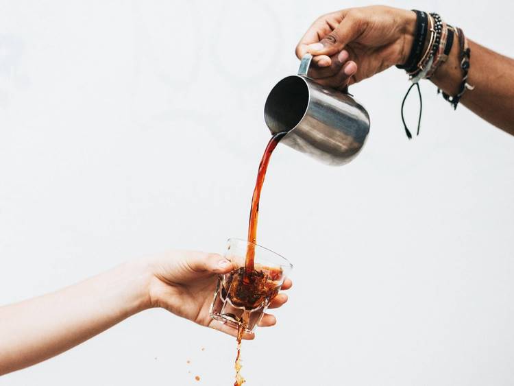 Coffee pouring from stainless steel caraffe into glass espresso cup and surface below