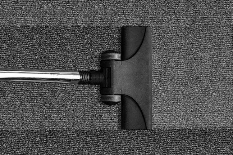 Miniature vacuum with black base and silver handle vacuuming gray carpeting