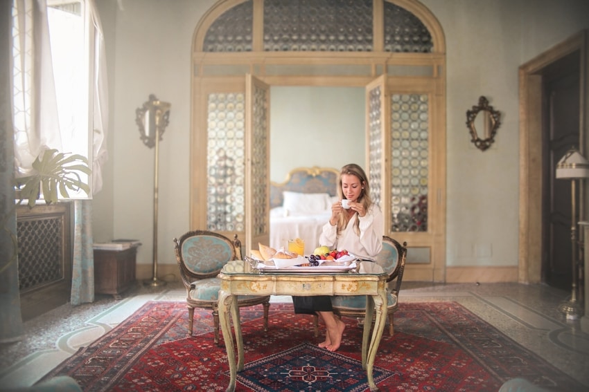 Woman sits at table in center of room with bare feet on beautiful Oriental rug