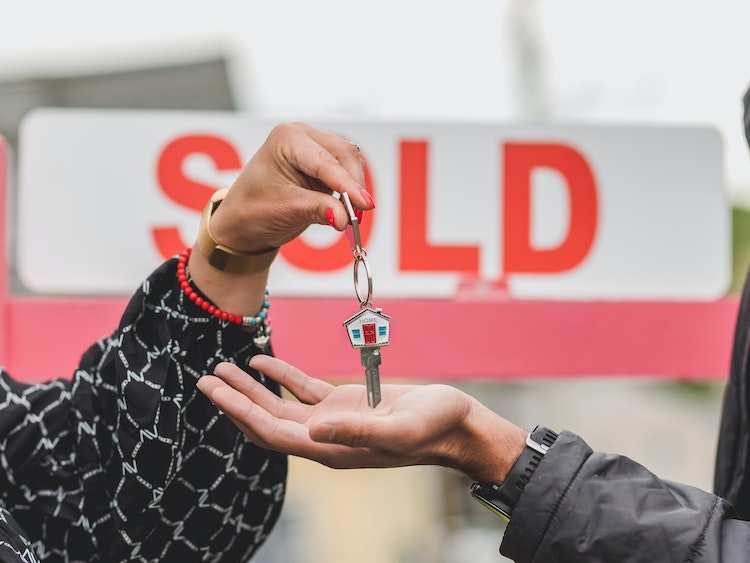 Realtor handing house key to new homeowner beside 'SOLD' sign in front yard