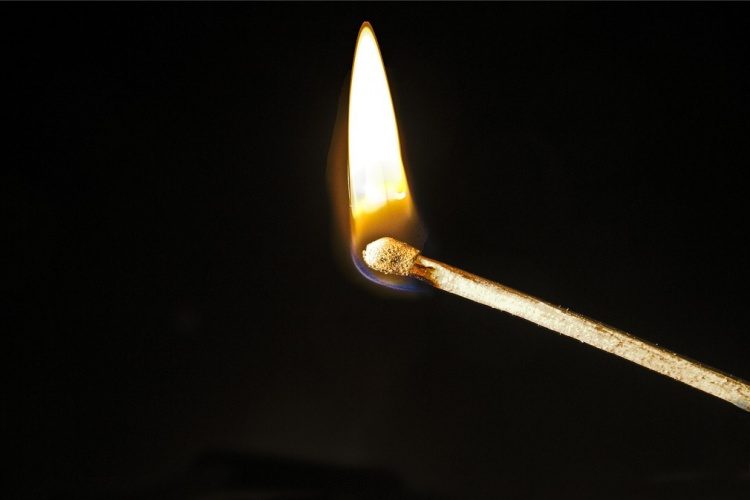 Close-up view of wooden match with lit flame against black background