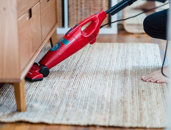 Cleaning rug in living room beneath wooden furniture with red vacuum