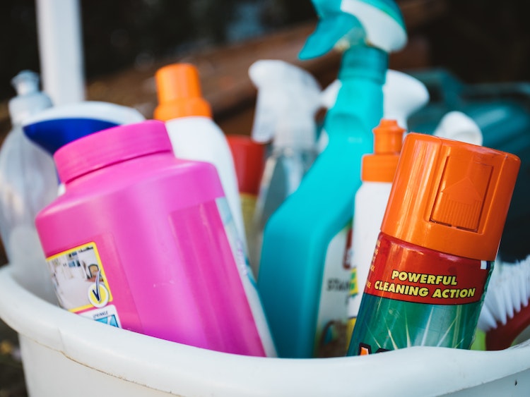 Assorted bottled cleaning supplies in gray bucket