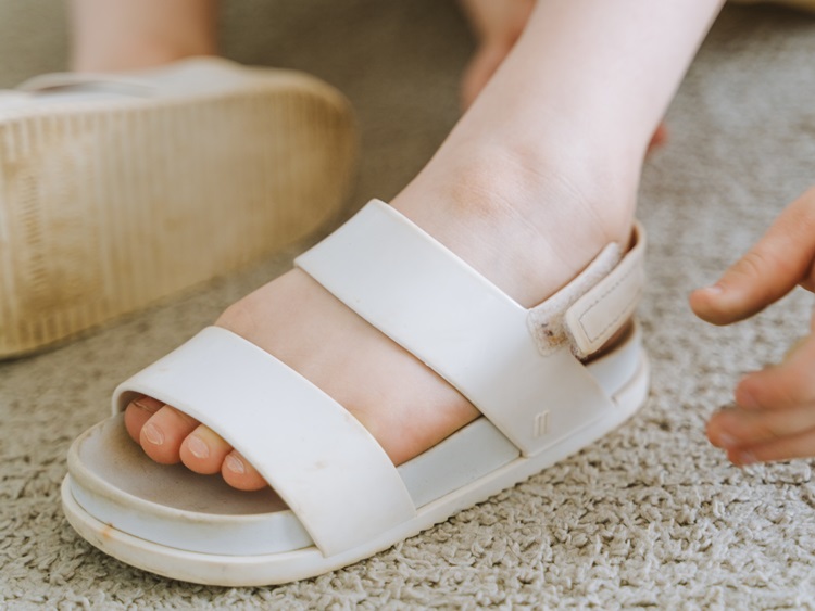 Close-up of child's feet in dirty white sandals on beige indoor carpeting