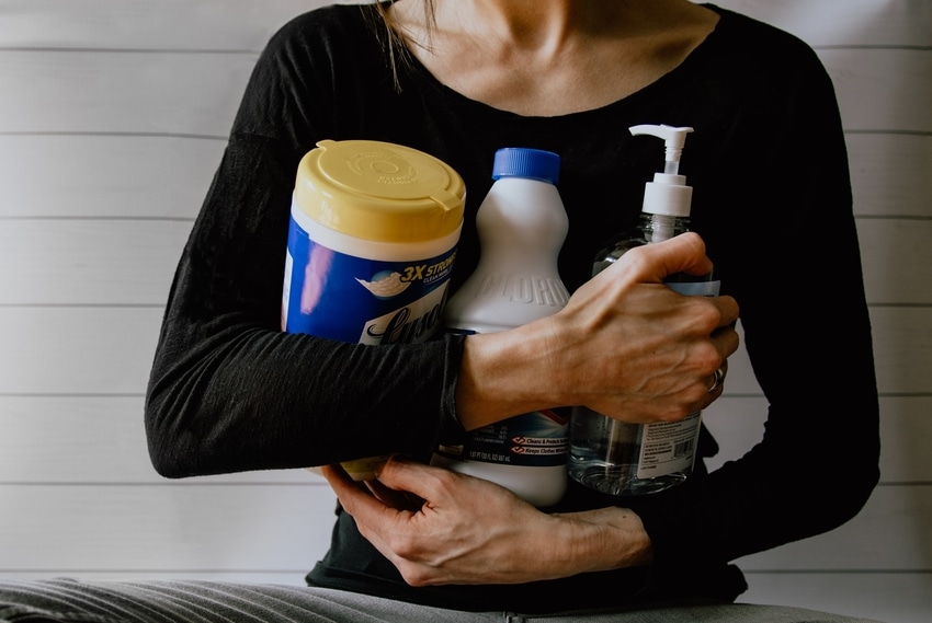 Woman in black long-sleeved shirt clutching cleaning products to chest before attempting DIY carpet stain removal