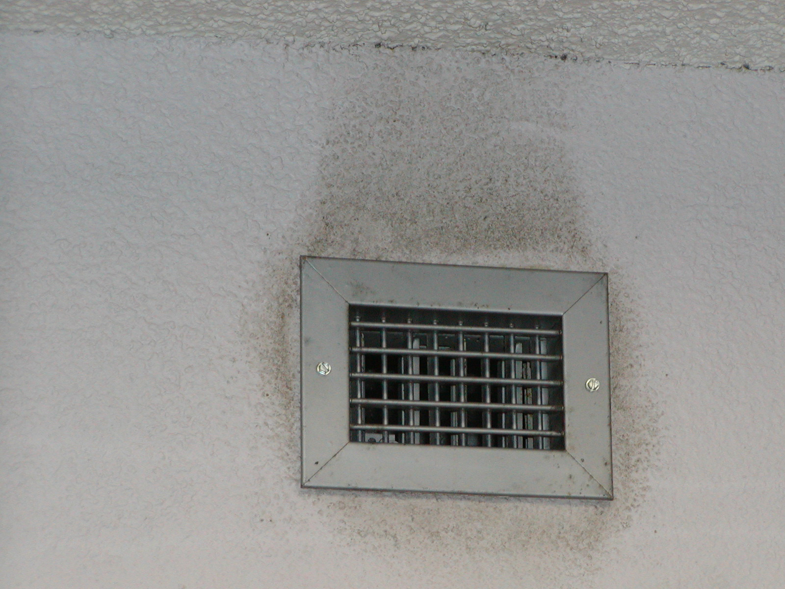 Dusty air vent near spackled ceiling of white room